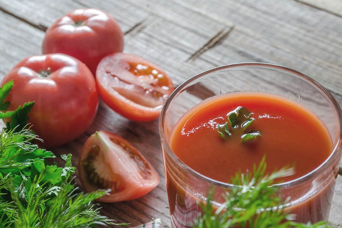 دو عدد گوجه‌فرنگی و یک عدد گوجه فرنگی قاچ شده بعلاوه‌ی یک لوان آب گوجه‌فرنگی تزئین شده با سبزیجات